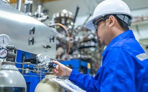 Technicien portant un casque et une combinaison bleue vérifiant un manomètre sur une installation industrielle