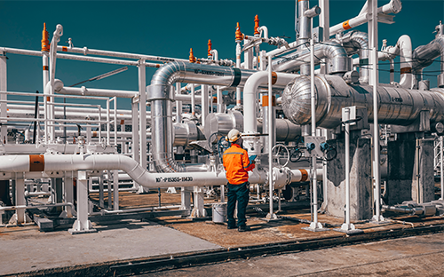 Technicien en tenue de sécurité contrôlant une installation industrielle de tuyauteries vapeur et d’équipements de mesure