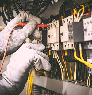 Techniker bei der Verkabelung eines Industrieschranks, mit Schutzhandschuhen und Energiezählmodulen