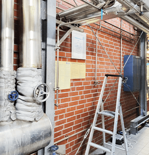 Промышленная установка с изолированными трубопроводами, клапанами и шкафом управления на кирпичной стене, иллюстрирующая условия эксплуатации пара.