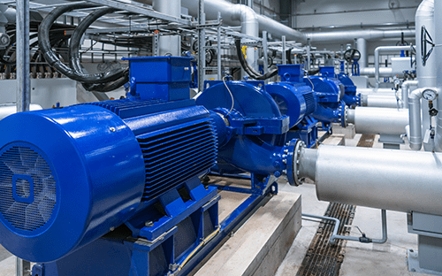 Line of blue industrial electric motors driving pumps on a piping system in an industrial environment