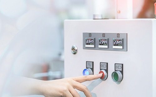 Рука, нажимающая на кнопку управления промышленного пульта с цифровыми дисплеями для контроля параметров процесса