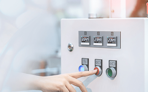 Mano di un operatore che preme un pulsante su un pannello industriale con regolatori di temperatura digitali integrati