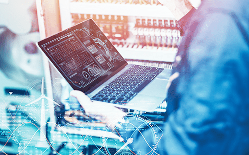 Techniker, der Energieverbrauchsdaten auf einem Laptop analysiert, mit digitalen Dashboards in einer industriellen Umgebung