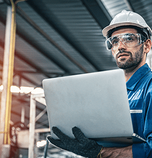 Tecnico industriale dotato di casco e occhiali di sicurezza che utilizza un computer portatile in un ambiente di produzione