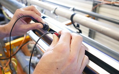 Technician performing an electrical test on a flow meter installed on a pipe to check and calibrate the measurement