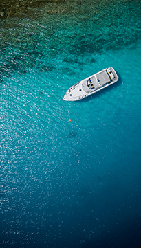Vista aérea de una lancha motora inmóvil sobre aguas turquesas cristalinas, encuadre vertical tipo viñeta.