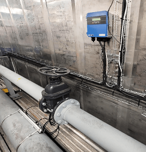 Flow meter installed on a chilled water pipe with wall-mounted electronic box