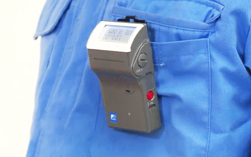 Elektronisches individuelles Dosimeter von Fuji Electric, das an der Tasche eines Arbeitskleidung befestigt wird, um die Strahlendosen im Strahlenschutz zu überwachen.