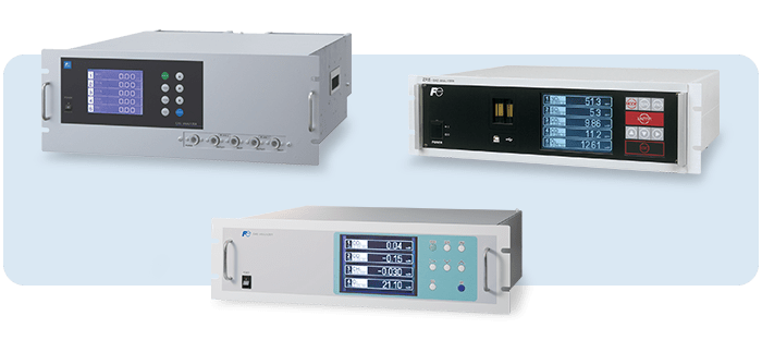 Três analisadores de gases industriais em rack com ecrãs digitais e painéis de comando