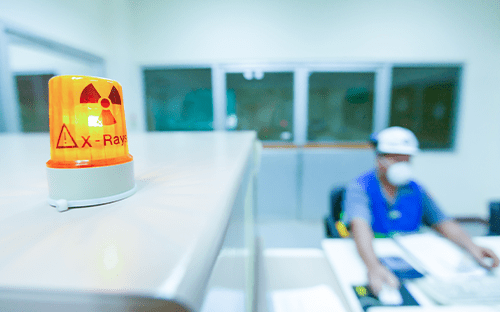 Orangefarbene Rundumleuchte mit Strahlungssymbol und der Aufschrift „X Ray“ im Vordergrund, die auf einen kontrollierten Bereich im medizinischen Umfeld hinweist.