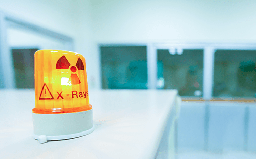 Orangefarbene Rundumleuchte mit Strahlungssymbol und der Aufschrift „X Rays“, die auf einen Bereich hinweist, in dem ionisierende Strahlung vorhanden ist.