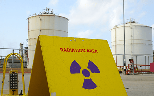 Gelbes Schild „Radiation Area“ mit Symbol für nukleare Gefahr vor Industrietanks an einem regulierten Standort