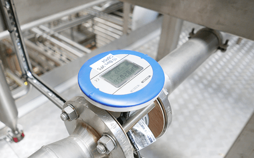 Ultraschall-Durchflussmesser, installiert an einer Druckluftleitung in einer industriellen Umgebung, mit gut lesbarem Digitaldisplay