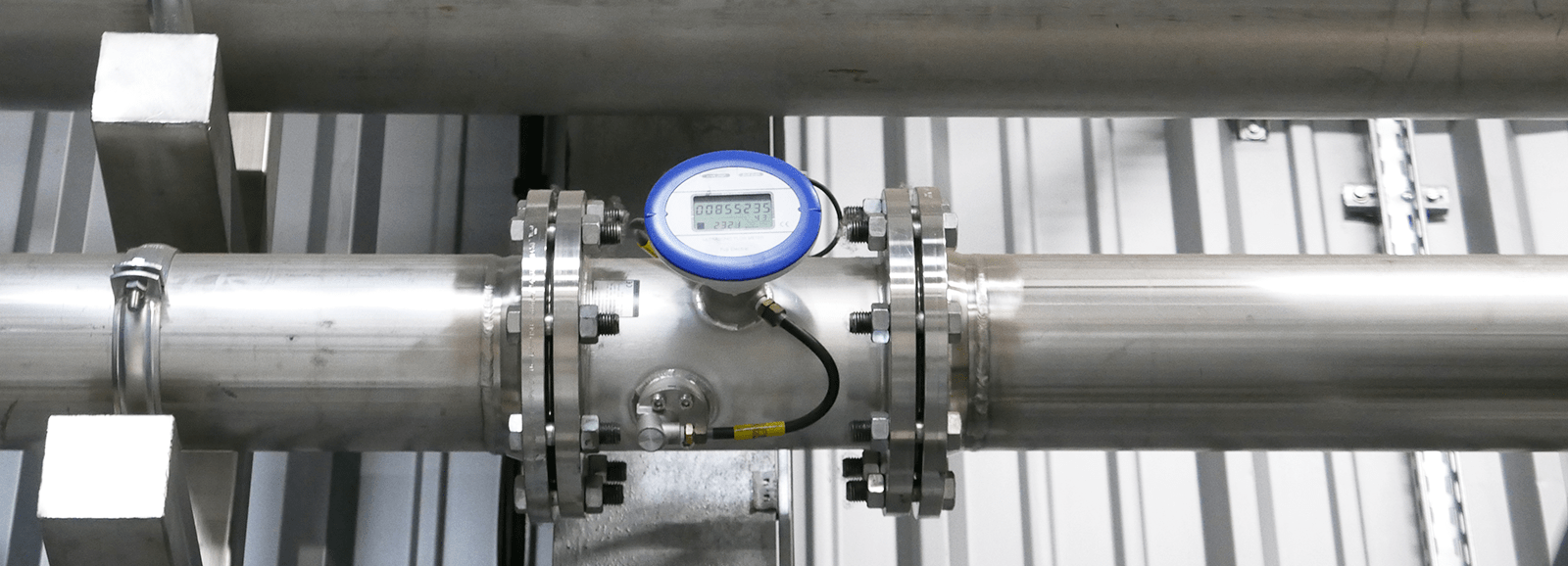 Ultraschall-Durchflussmesser, installiert an einer industriellen Stahlrohrleitung mit Flanschen und zentral angeordnetem Digitaldisplay