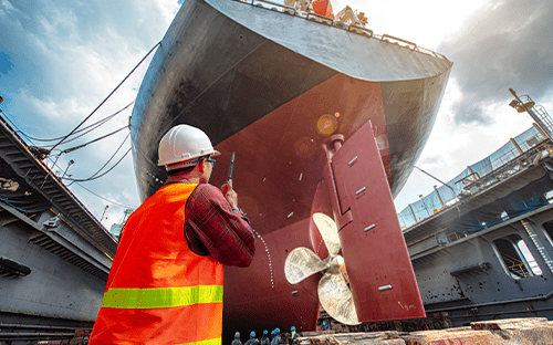 Ein Techniker in einer Warnweste inspiziert während Wartungsarbeiten den Propeller eines Schiffes im Trockendock