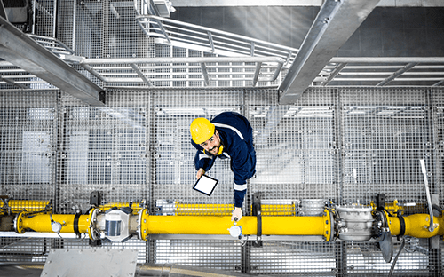 Techniker bei der Inspektion einer Industrieleitung mit einem Sensor an einer Druckluftleitung in einer technischen Anlage