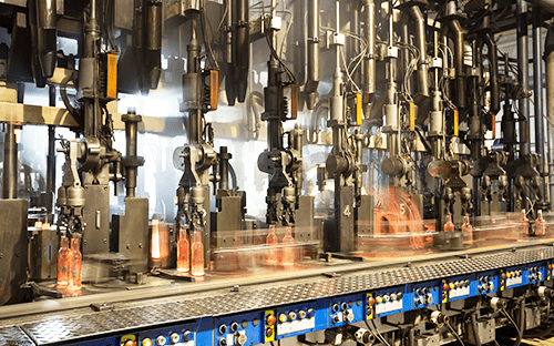 Industrielle Produktionslinie mit automatisierten Maschinen, die erhitzte Glasflaschen auf einem Förderband handhaben