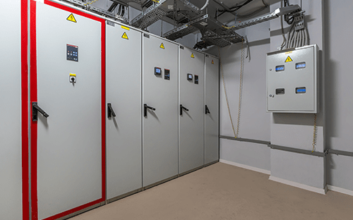 Teknik odada kontrol panelleri ve güvenlik işaretlemeleri bulunan endüstriyel elektrik panoları