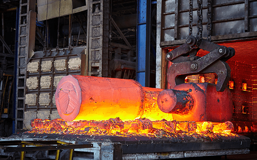 Раскаленный стальной заготовка, перемещаемая механическими клещами на выходе из промышленной печи для термообработки