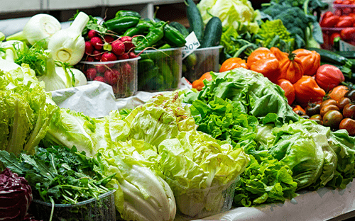 Bancada de legumes frescos com saladas, rabanetes, pimentos e ervas aromáticas, mostrando produtos conservados em ambiente controlado