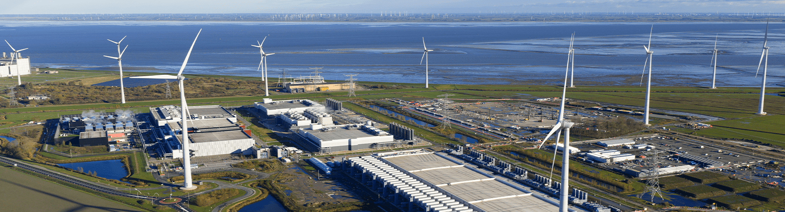 Kıyı şeridine yakın bir bölgede rüzgar türbinleri ve teknik binaların bulunduğu bir sanayi kompleksinin havadan görünümü