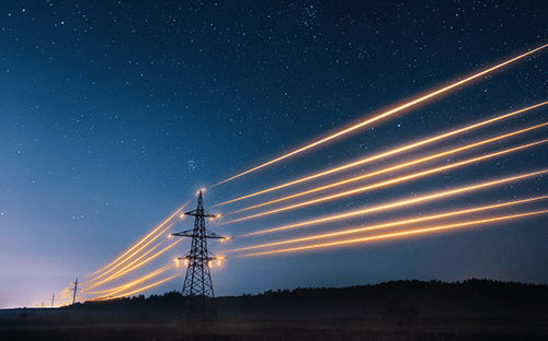 Gece manzarasının üzerinde ışık izleri bırakarak enerji taşıyan yüksek gerilim elektrik hatları
