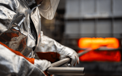 Оператор, работающий с алюминиевым комбинезоном и занимающийся обработкой металлических прутков рядом с печью для термообработки