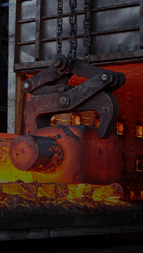 A chain-suspended handling clamp gripping a heated steel billet as it exits an industrial furnace