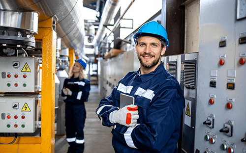 Техник в защитной одежде и синем шлеме, держащий планшет, в промышленной среде с контрольно-измерительным оборудованием