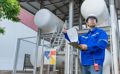 Técnico com equipamento de segurança a inspecionar uma instalação industrial de azoto, com reservatórios e documentos de controlo na mão