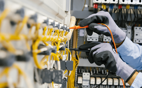 Techniker, der mit einem Messgerät die elektrischen Anschlüsse in einem Schaltschrank überprüft