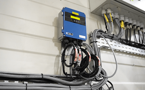 Elektronischer Durchflussmesser, installiert an einer Technikwand mit industrieller Verkabelung zur Überwachung des Wasserverbrauchs