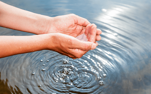 Hände, die Wasser über einer welligen Fläche auffangen, als Symbol für den Schutz und die Bewirtschaftung der Wasserressourcen