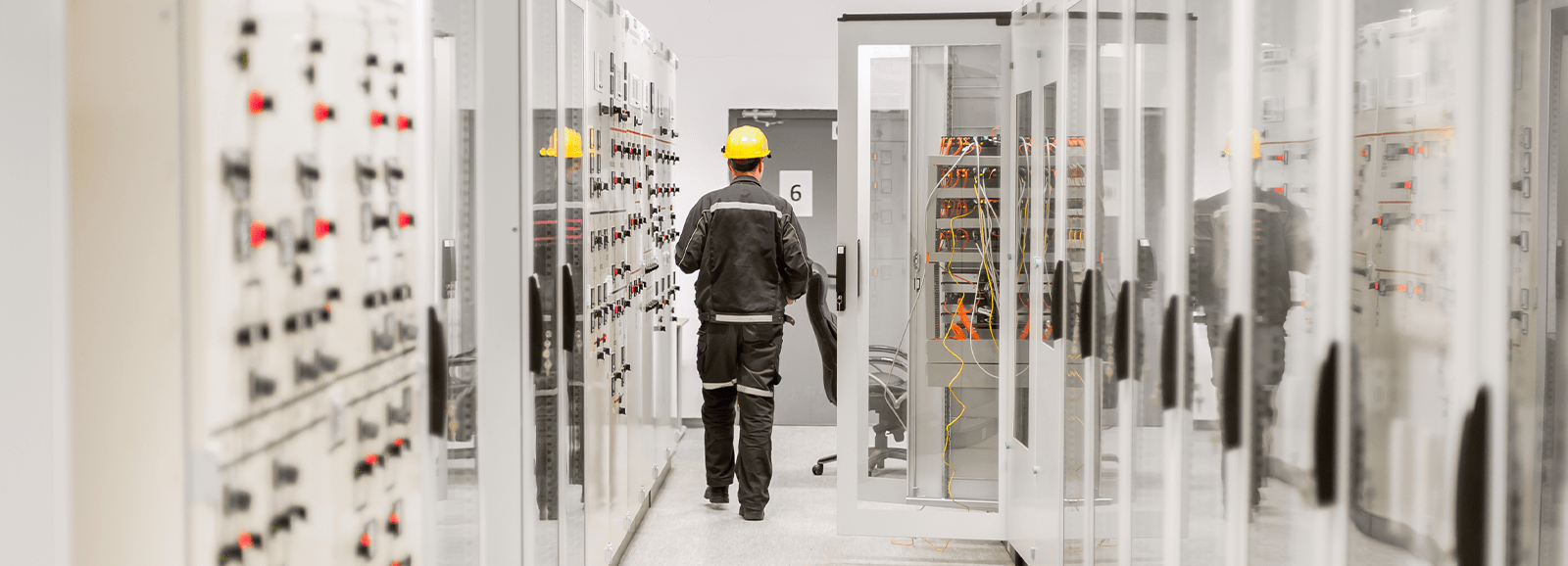 Techniker, der sich in einem elektrischen Kontrollraum bewegt, der mit Schaltschränken und Überwachungssystemen ausgestattet ist