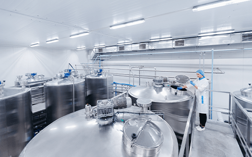 Edelstahltanks in einer industriellen Produktionshalle, in der eine Mitarbeiterin eine Überprüfung der Anlagen durchführt
