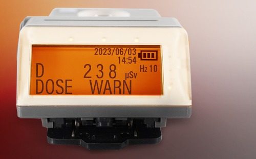 Dosimètre électronique personnel affichant un avertissement de dose avec écran rétroéclairé orange et valeur mesurée