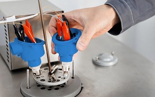 Techniker, der zwei an einen Kalibrierungsstand angeschlossene Temperatursonden handhabt, um deren Messgenauigkeit zu überprüfen