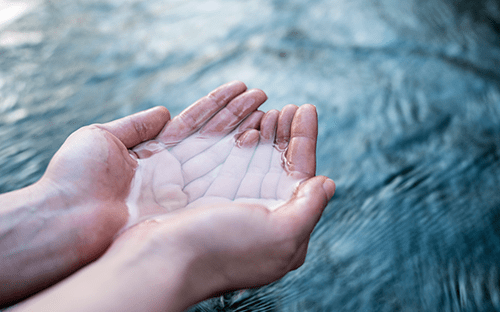 Mains recueillant de l’eau claire au-dessus d’une surface aquatique, illustrant la préservation et la gestion durable de la ressource