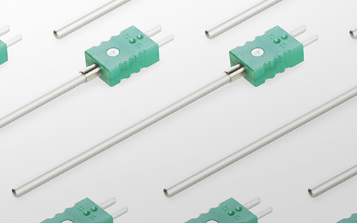 Motiv aus mehreren Thermoelement-Temperaturfühlern mit grünen Steckern auf hellem Hintergrund