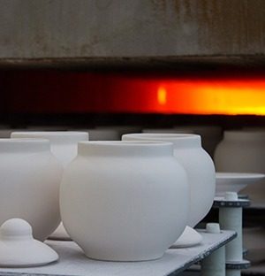 Weiße Keramikteile auf einer Produktionslinie vor einem industriellen Hochtemperaturofen