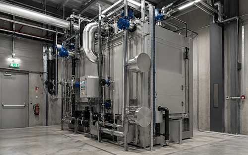 Instalación industrial de recuperación de calor con intercambiadores, tuberías y válvulas para optimizar la eficiencia energética de un horno crematorio