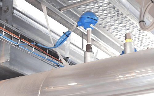 Temperaturfühler mit blauem Anschlusskopf, installiert an einer wärmeisolierten Industrierohre