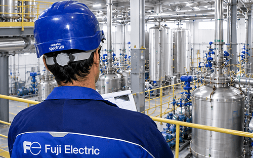 Technicien Fuji Electric observant une installation industrielle équipée de cuves et de tuyauteries pour le pilotage des procédés