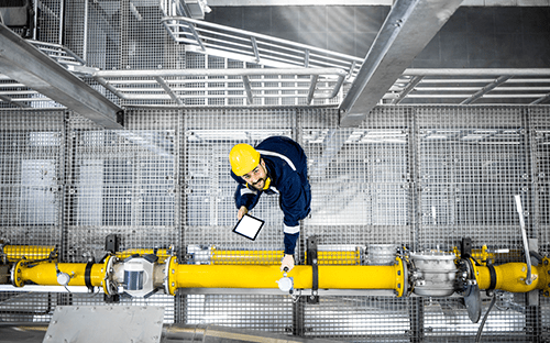 Technicien portant un casque de sécurité inspectant une conduite industrielle équipée d’un instrument de mesure avec une tablette