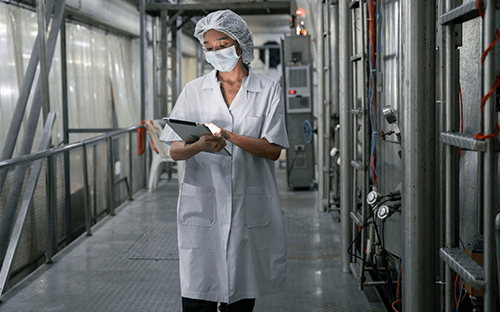 Technicienne en tenue de protection utilisant une tablette dans une installation industrielle pour le suivi des &eacute;missions