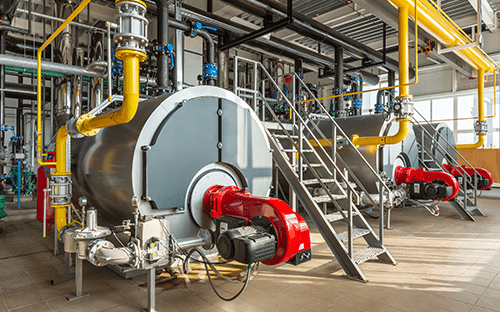 Zwei mit Brennern ausgestattete Industriekessel, umgeben von Rohrleitungen und Prozessanlagen