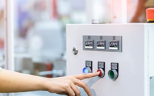 Bediener, der einen Knopf an einem Schaltschrank betätigt, der mit drei Temperaturreglern ausgestattet ist