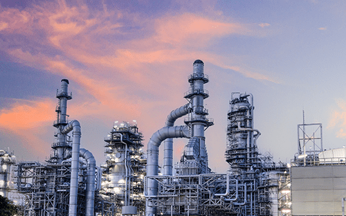 Industriegelände mit Türmen, Rohrleitungen und Aufbereitungsanlagen unter einem farbenprächtigen Himmel bei Sonnenuntergang