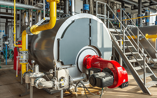 Chaudière industrielle cylindrique équipée d'un brûleur rouge, d'une conduite jaune et de tuyauteries dans une chaufferie